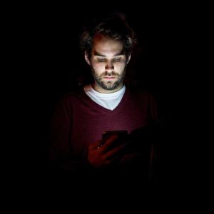 Man scrolling on his phone in the dark.